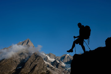 Silhouette hiking man with backpack and trekking pole, over European Alps on the background.