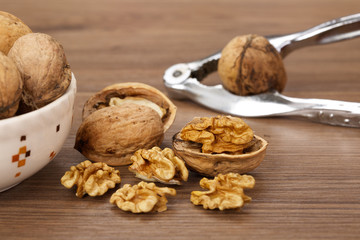 Close-up of cracked walnuts with nutcracker on light wooden background