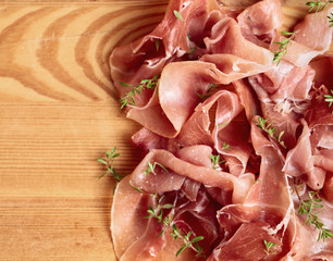 Italian prosciutto crudo or jamon with thyme on a wooden table.