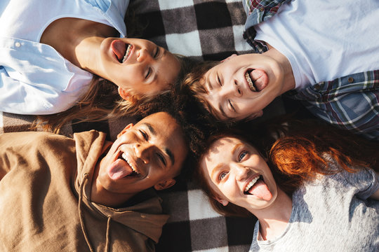 Image of stylish friends men and women laughing, and lying on blanket in circle outdoor