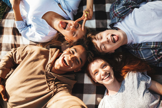 Multiethnic young people guys and girls laughing, and lying on blanket in circle outdoor