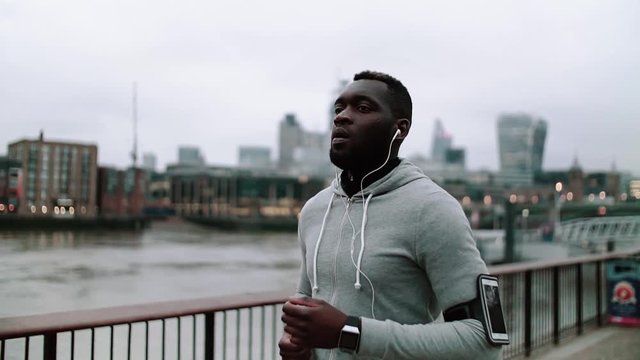 Young sporty black man runner with smart phone running on the bridge in a city.