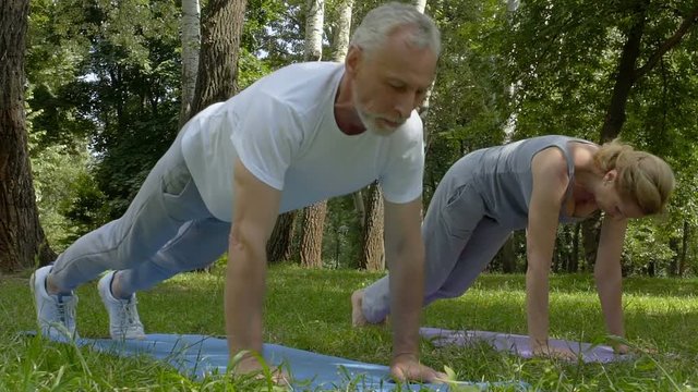 Active senior people doing push-ups and yoga asanas in park, slow motion