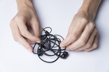 Female hands unravel the black little headphones on a white background