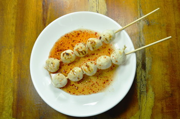 grilled pork ball stabbing in wooden stick dressing spicy and sweet sauce on plate