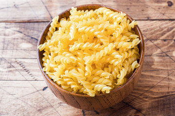 Raw pasta in a wooden bowl on a rustic wooden background.