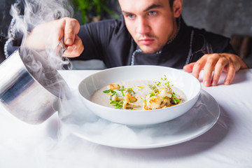 Cook chef making creme soup with herbs, mushrooms, scallops and toast bred - added dried ice for...