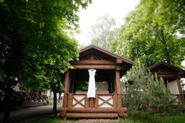 Beautiful white casual wedding dress hanging on the balcony of the wooden house in the forest. Wedding day