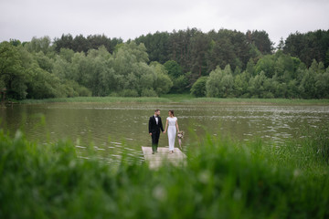 Beautiful happy wedding couple of groom and bride walking holding hands on the pier near the lake. Wedding day concept