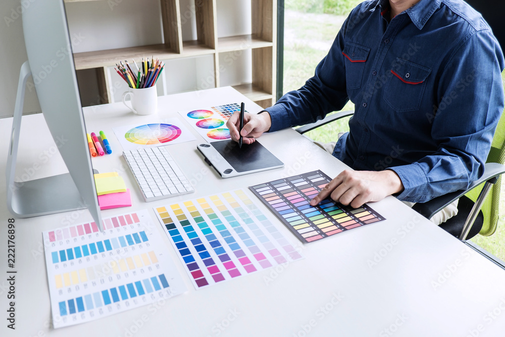 Poster Image of male creative graphic designer working on color selection and drawing on graphics tablet at workplace with work tools and accessories