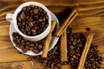 Coffee beans in white cup and cinnamon sticks on wooden table. Top view