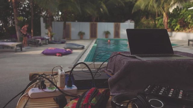 Background with dj deck opposite pool and people next to it. people swimming in the pool