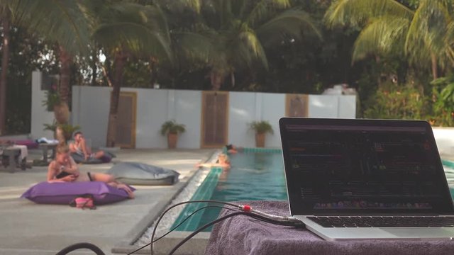 Background with a dj's laptop opposite people in the pool and next to it