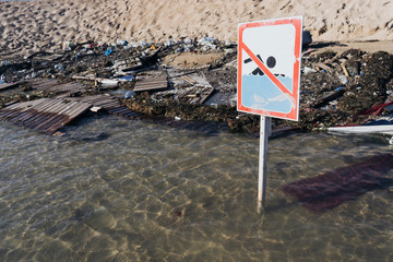 Sign prohibiting swimming on the beach. A sandy beach sign on a wooden column is thrust into the...