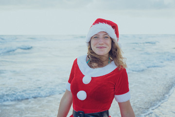 Obraz premium Girl dressed as Santa Claus standing on the beach or ocean. New year holidays concept. Happy New Year and merry Christmas! 