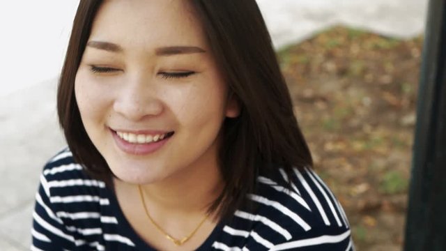 Close up portrait of young Asia woman smiling with black hair blowing in wind looking and blur background slow motion