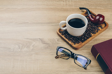 a cup of coffee with a pile of coffee beans and a tobacco smoking pipe in the wooden tray, a red...