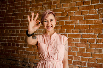 Young beautiful girl on a brick wall background shows ok sign