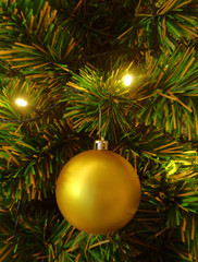 Fototapeta na wymiar Vertical photo of a shiny gold ball shaped Christmas ornament hanging on sparkling Christmas Tree 