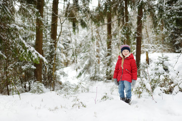 Adorable little girl having fun in beautiful winter forest. Happy child playing in a snow.