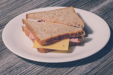 Delicious cheese sausage sandwich on a white round plate. Wooden background, horizontal view, vintage effect
