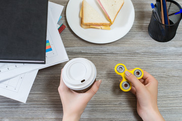 Concept of having a break at work. Top view photo of hands holding fidget spinner and cup of coffee
