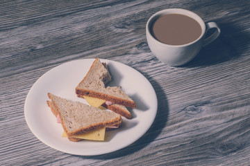 Lunch at work. Close up of bitten cheese sandwich on a white round plate and cup og hot coffee
