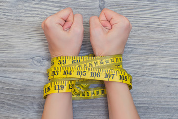 Concept of lossing weight. Woman's hands tied with yellow tape measure.