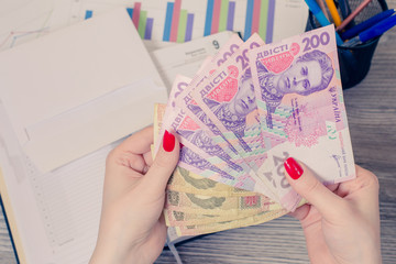 Woman's hands holding a lot of Ukrainian money over desktop