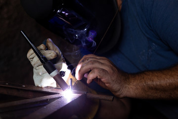 A man with protective helmet welding two pieces of metal. - obrazy, fototapety, plakaty