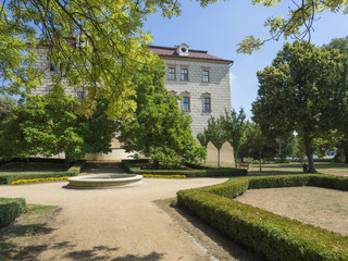 Renaissance style castle with Sgraffito decorated facade, park, footpath, green trees garden, fountain and wooden bench, sunny summer day