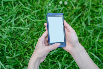 Hands holding mobile phone with empty screen over grass background