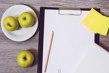Close up of office accessorise: clipboard, a plate of apples, blank notepad on a wooden background