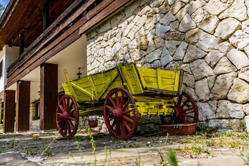 Close-up of part of a building with a stone wall and an old cart in yellow and brown. A rural house with large pieces of cut stone. Texture, background.