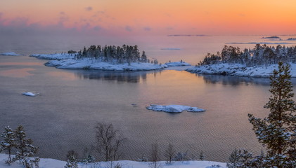 Fototapeta premium A colorful sunset on the Ladoga lake in the frost. Winter day. Open water hovers from frost. Islands in the snow.