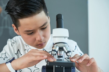 Curious Asian boy putting glass slide into microscope
