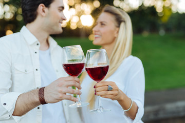 To our future. Glasses with red wine being clinked together by joyful happy couple while having a celebration