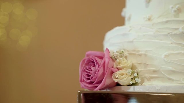 Close up of a white wedding cake with Mickey Mouse designs on it and pink and white flowers.