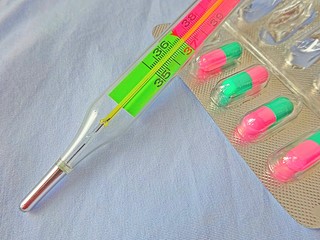 Medicine Medical Pharmacy Health Care Help Colored Scale Glass Thermometer Temperature Measuring Tool and Pilules Pills Tablets Drugs Antibiotics On The Blue Background and Copy Paste Text Space