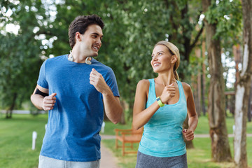 Great mood. Cheerful happy nice couple smiling to each other while jogging together in the woods