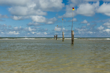 A row of poles marking the swimming area leading into the North Sea in Norderney with cloudy blue...