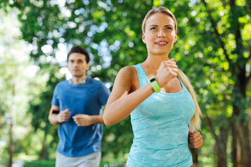 Sports exercise. Delighted nice woman being in the park while jogging in the morning