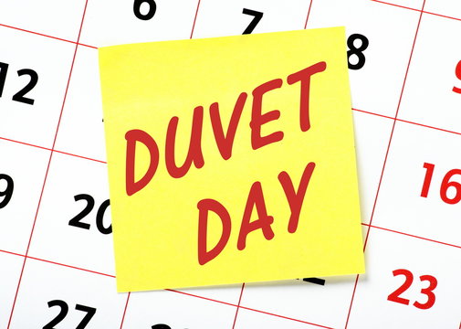 The words Duvet Day on a yellow sticky note with a calendar behind as a reminder to take leave from work