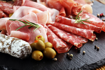 Marble cutting board with prosciutto, bacon, salami and sausages on wooden background. Meat platter