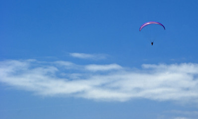 A paratrooper flies against a blue cloudy sky