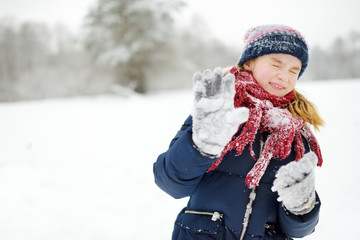 Adorable little girl having fun in beautiful winter park. Cute child playing in a snow.