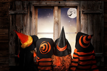 Halloween.Children in costumes of witches and wizard  at night sit near a window andand look at the...