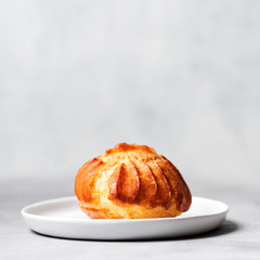 Close up of large delicious profiteroles with custard served on a white plate on a gray background.