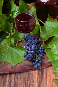 Red wine in a glass. A bunch of blue grapes next to it on the wooden table