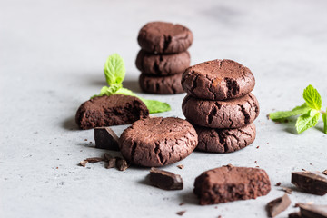 Chocolate cookies with pieces of chocolate and mint on a grey concrete background. Selective focus.